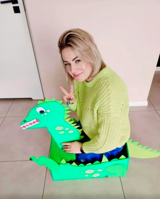 Opiekunka z dinozaurem wykonanym z kartonu podczas zajęć kreatywnych